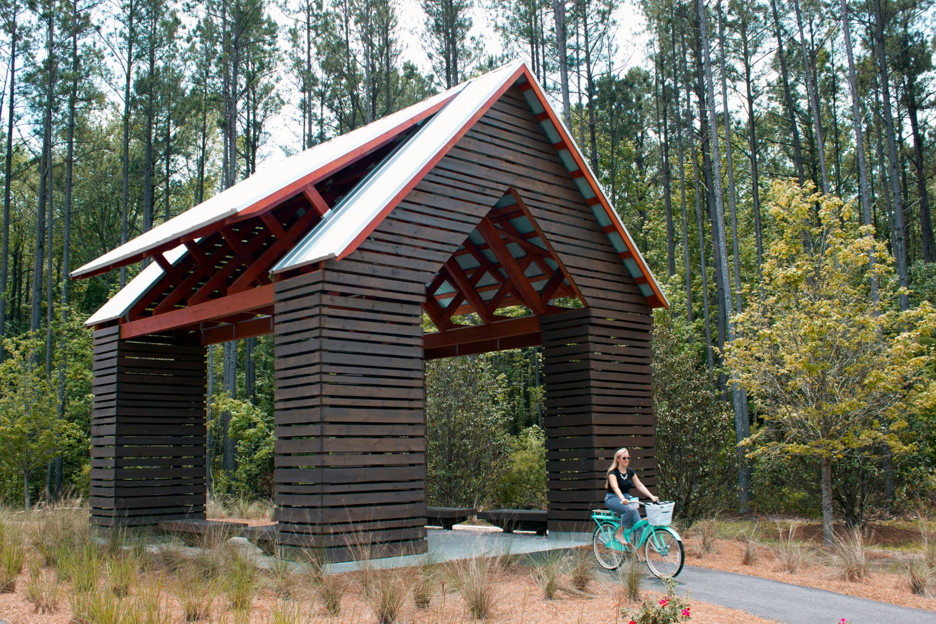 Cyclist riding under a timber folly on a pine-shaded Nexton trail